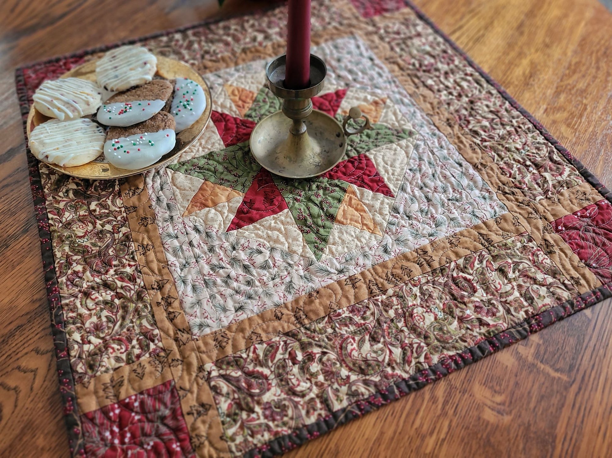 Christmas star centrepiece quilt on a wooden table with a candle and cookies on a plate.