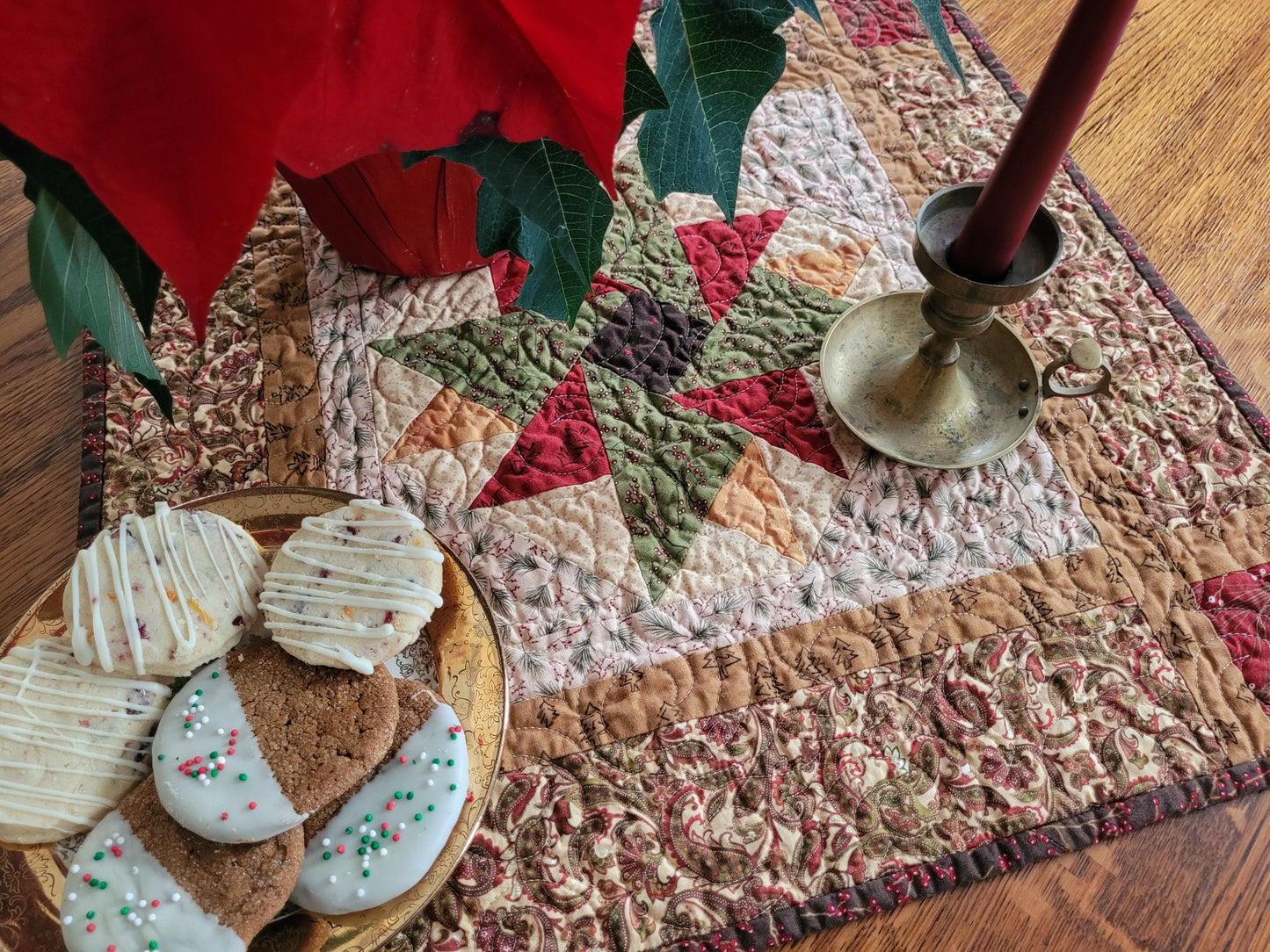 Stylized quilt on tabletop with Christmas cookies, poinsettia and a candle.