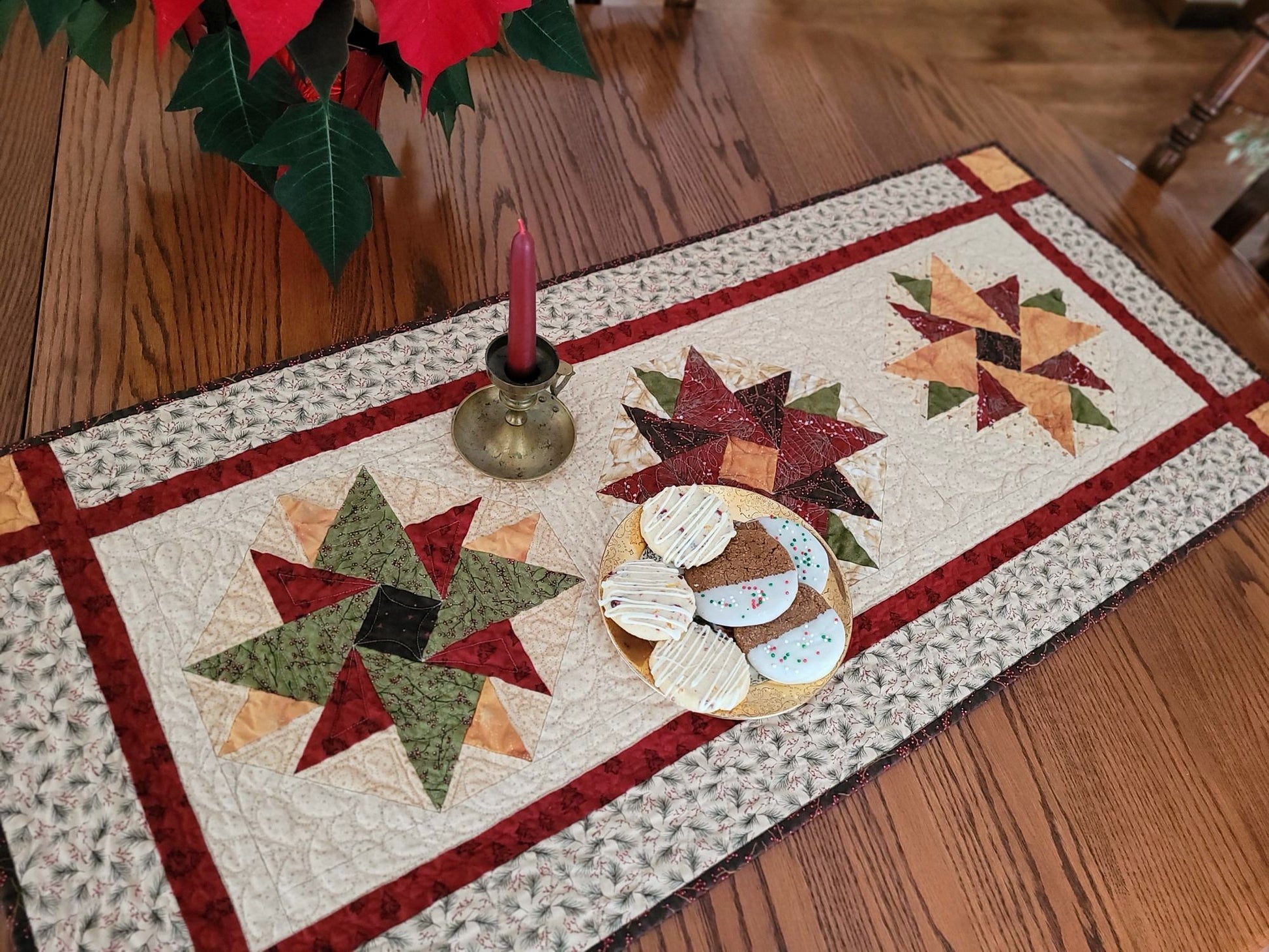 Quilted table runner with star patterns on a wooden table with a candle and poinsettia in background