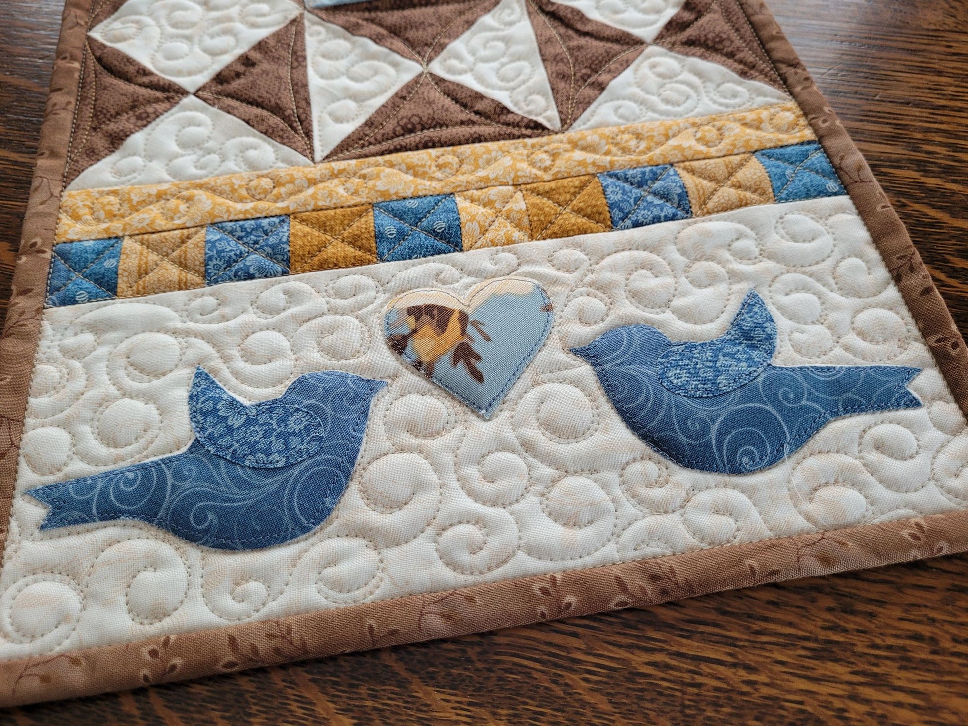 Close up of applique blue birds, floral heart and custom quilting on the Love Birds table runner.