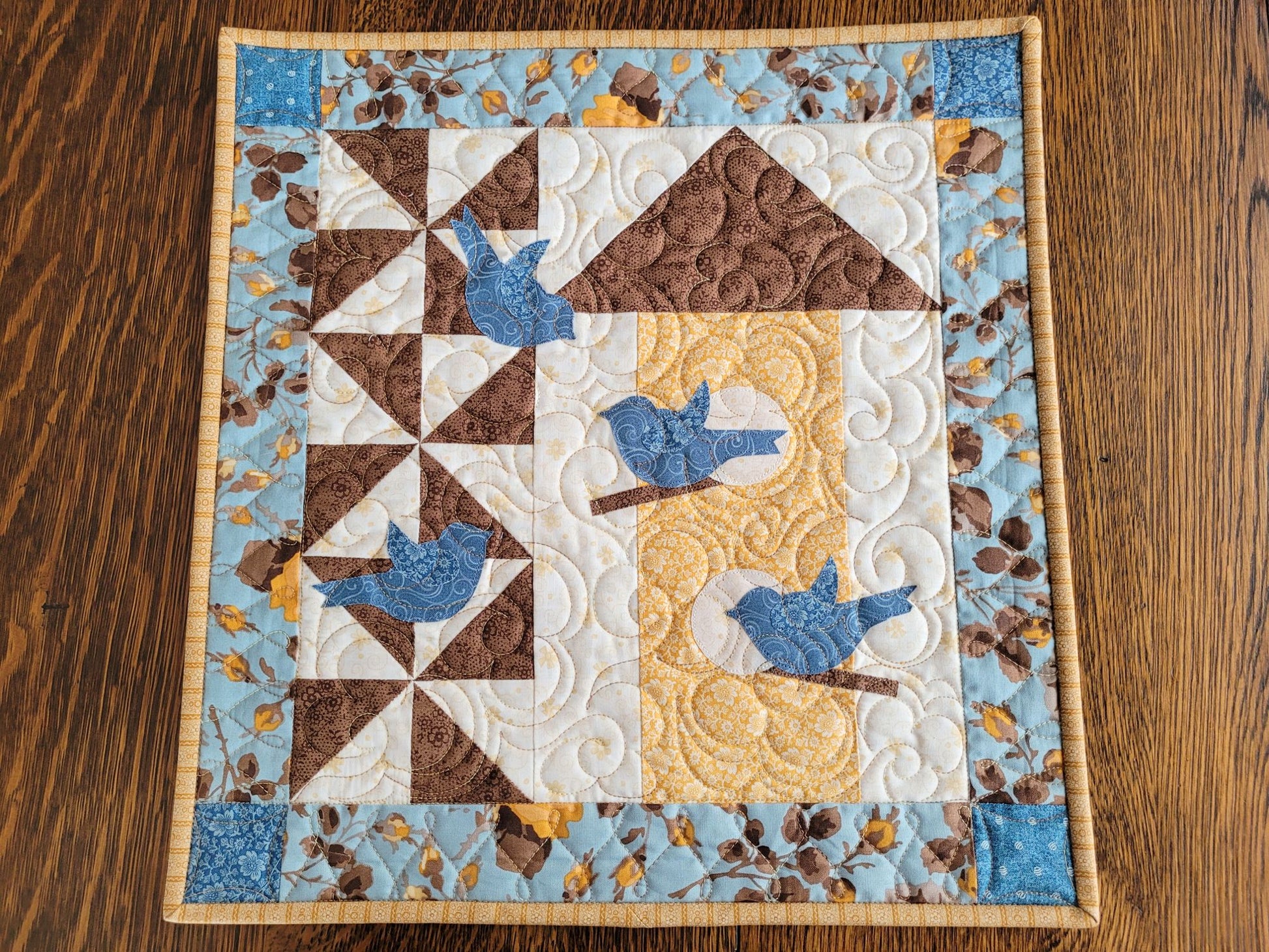 Wall quilt with blue birds and birdhouse design on a wooden surface