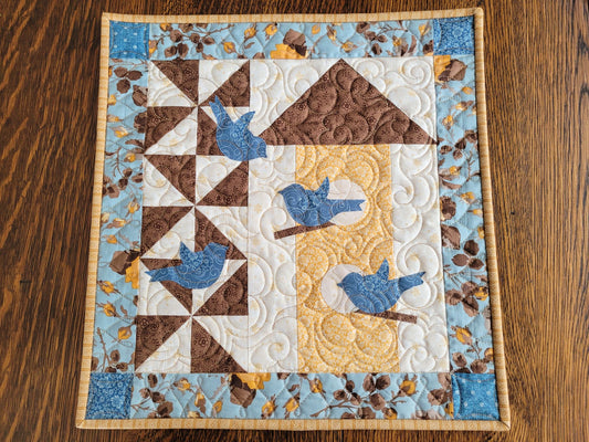 Wall quilt with blue birds and birdhouse design on a wooden surface