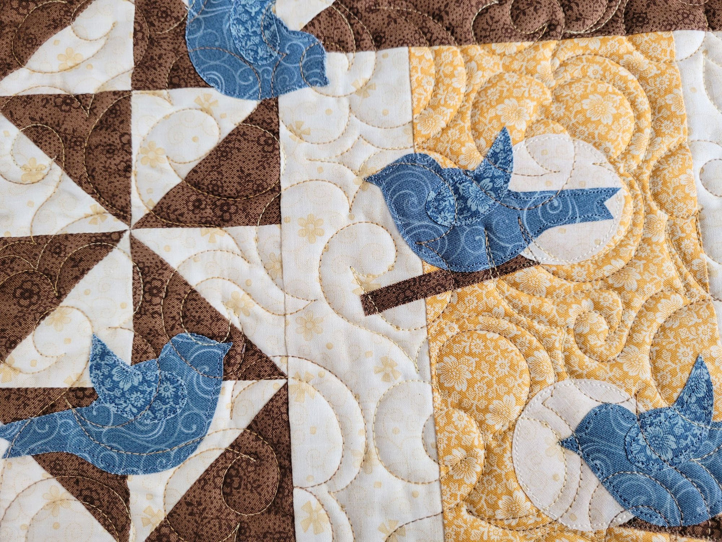 Close up of applique blue birds around the birdhouse, showing the subtle floral fabrics and freemotion stitching on the Thoughts of Spring Wall Quilt.