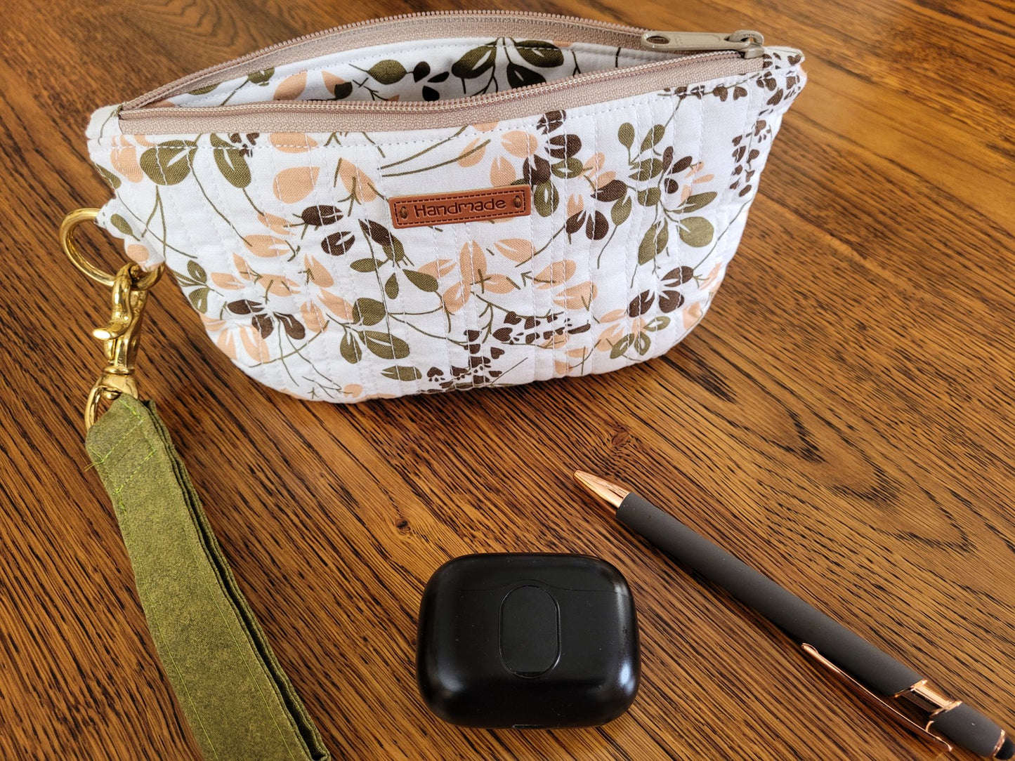 Quilted zipper pouch in leafy fabric on a wooden surface.