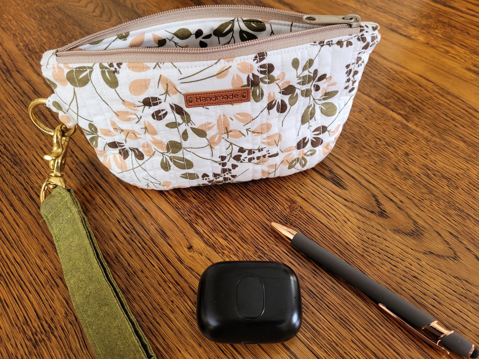 Quilted zipper pouch in leafy fabric on a wooden surface.