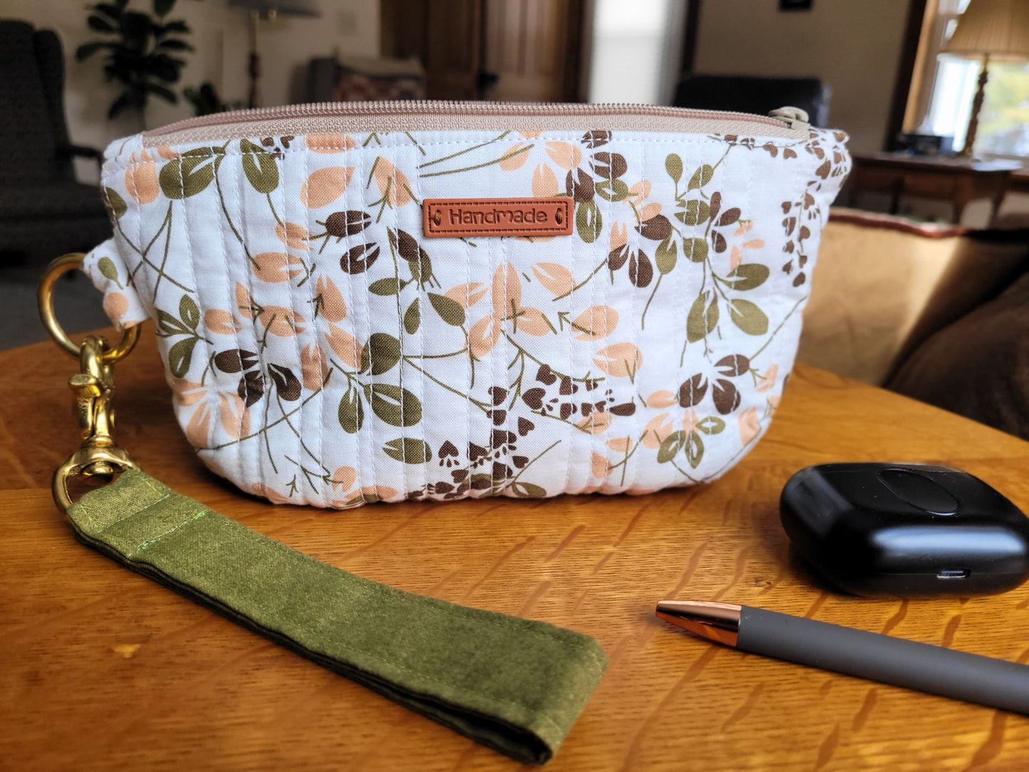 Leaf-patterned pouch with a green wrist strap on a wooden surface