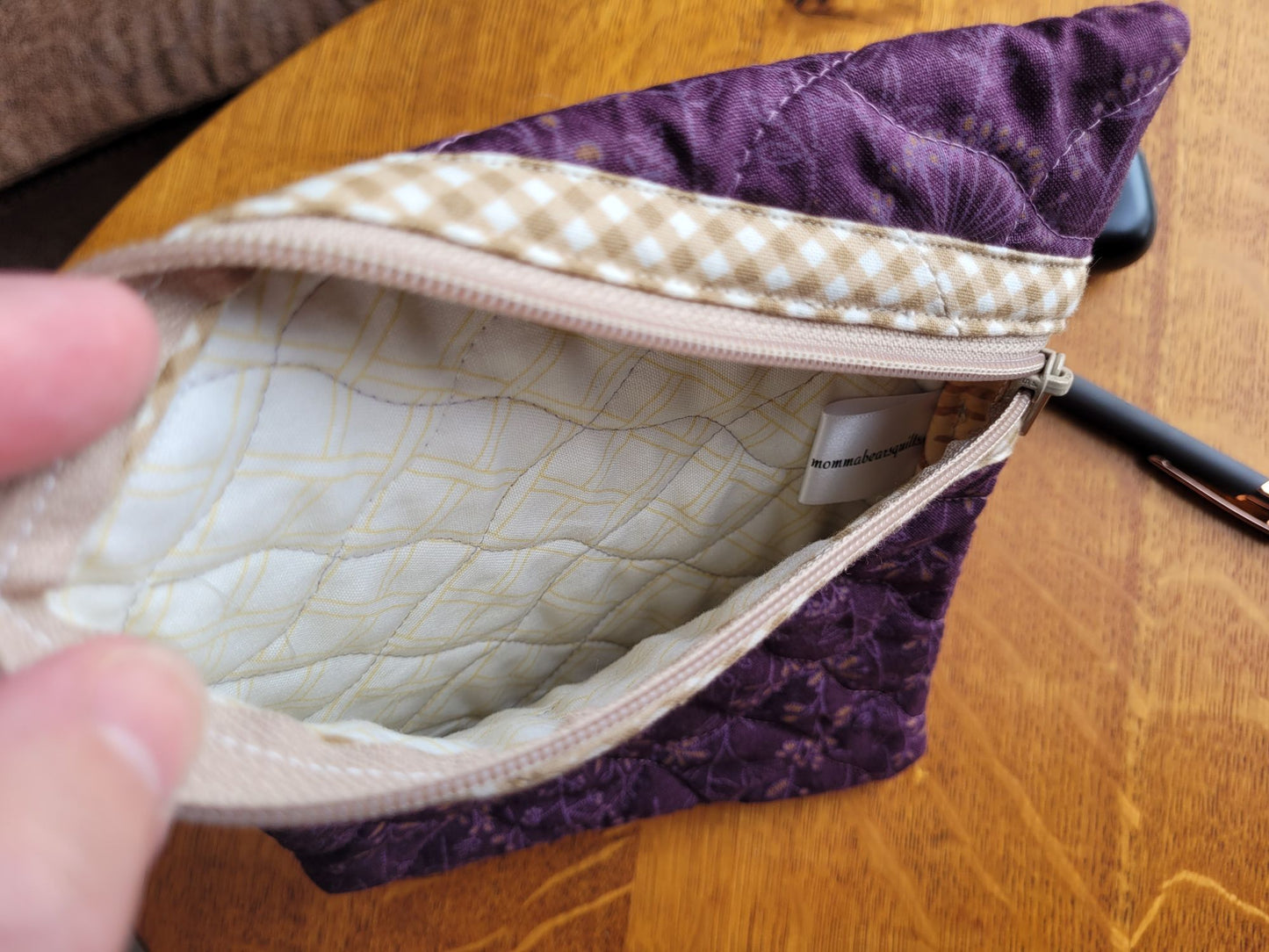 Purple quilted pouch with beige interior on a wooden surface