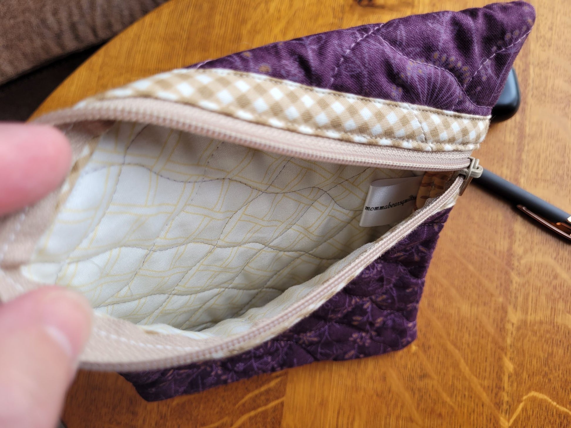 Purple quilted pouch with beige interior on a wooden surface