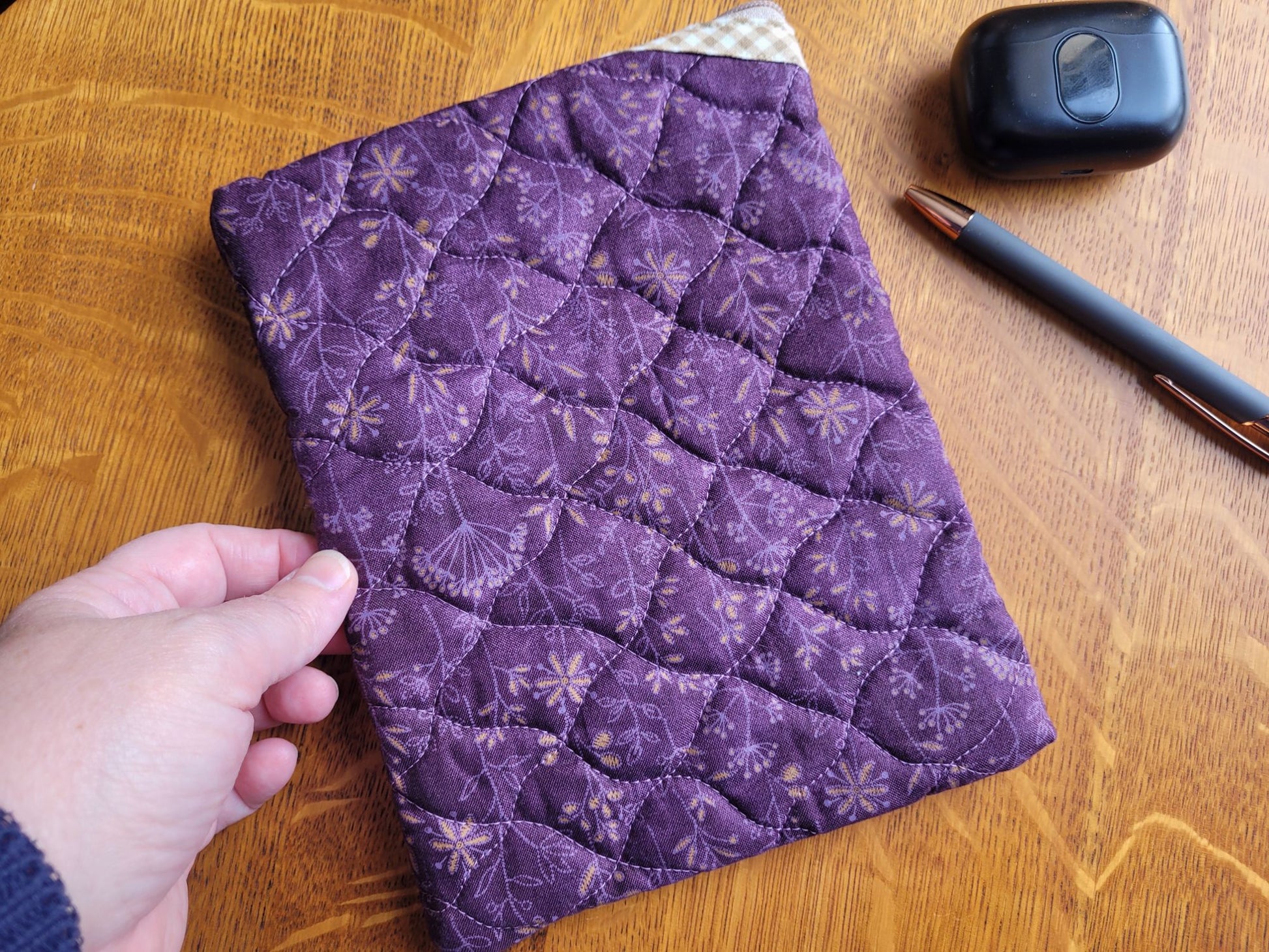 Back of purple quilted pouch on a wooden surface with a hand touching it