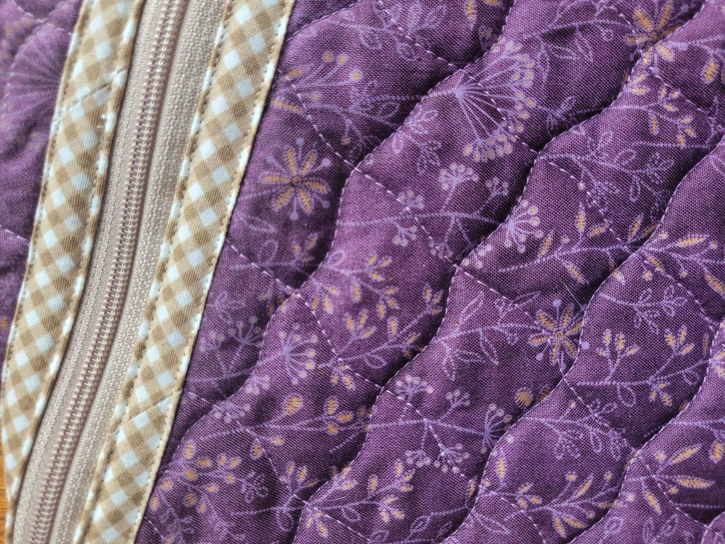 Close-up of a purple quilted fabric with floral patterns and a zipper.