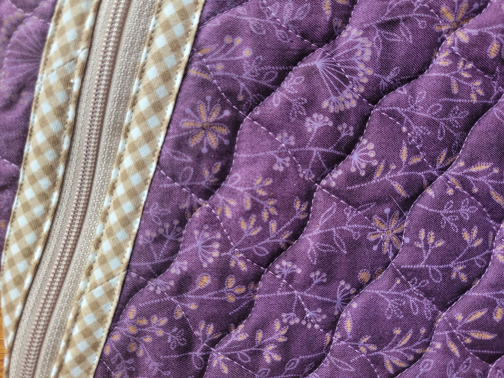 Close-up of a purple quilted fabric with floral patterns and a zipper.