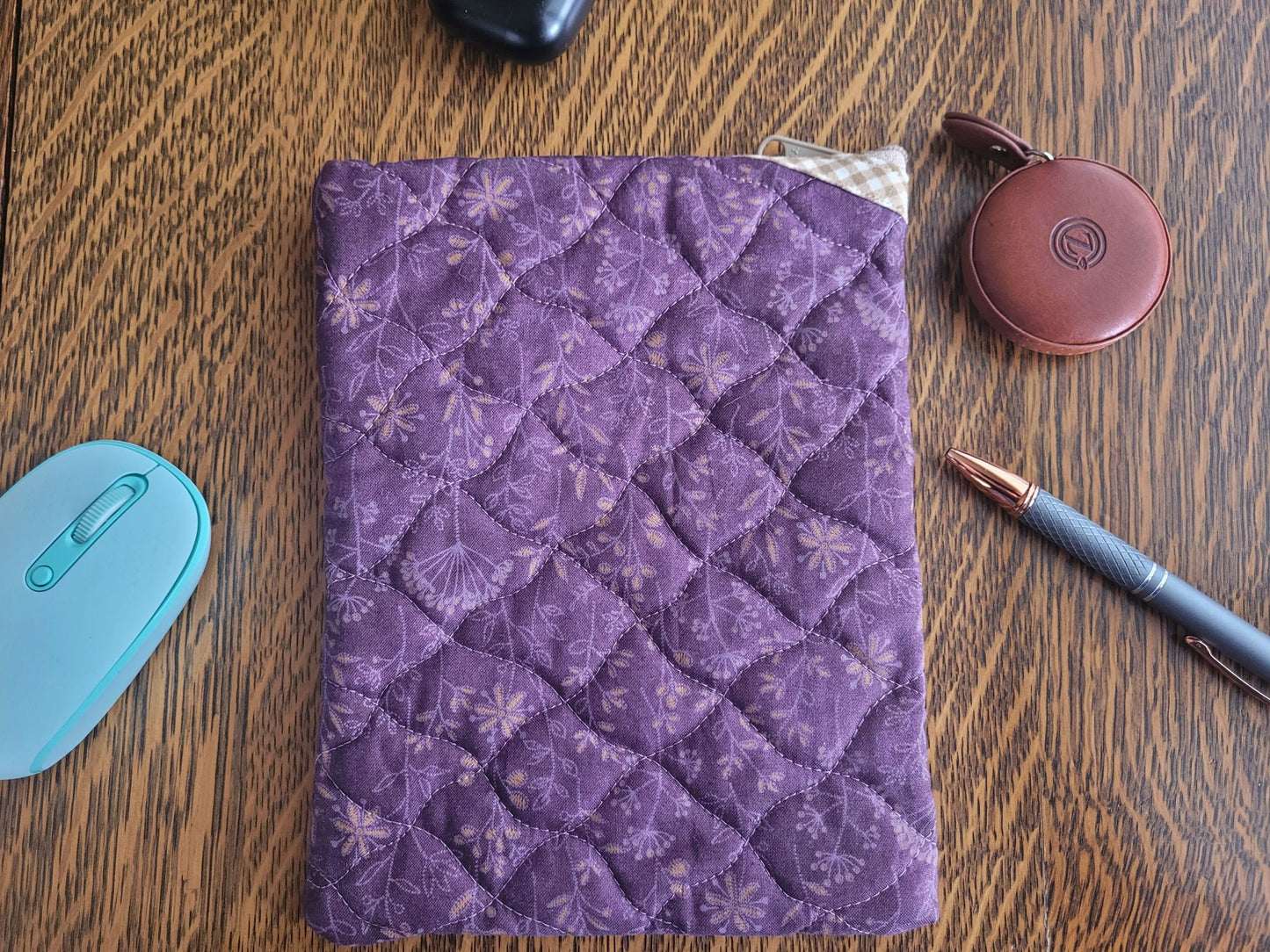 Showing back of purple quilted bag on a wooden surface with a pen, mouse, and small round container.