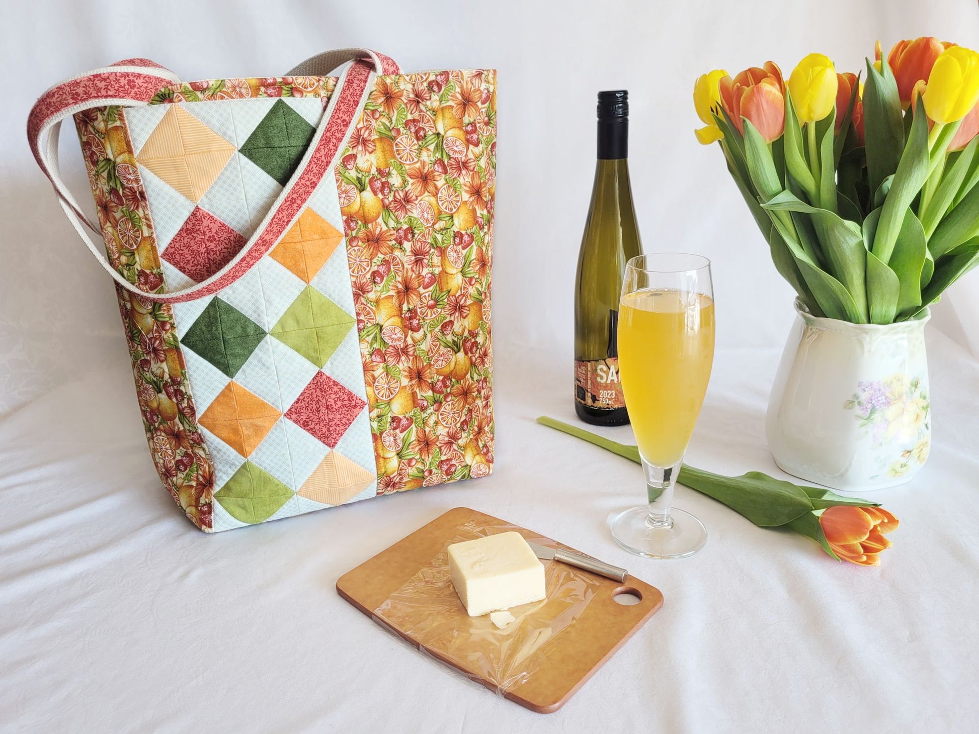 Quilted picnic tote on table with a cheese board, wine bottle and glass, and tulips.