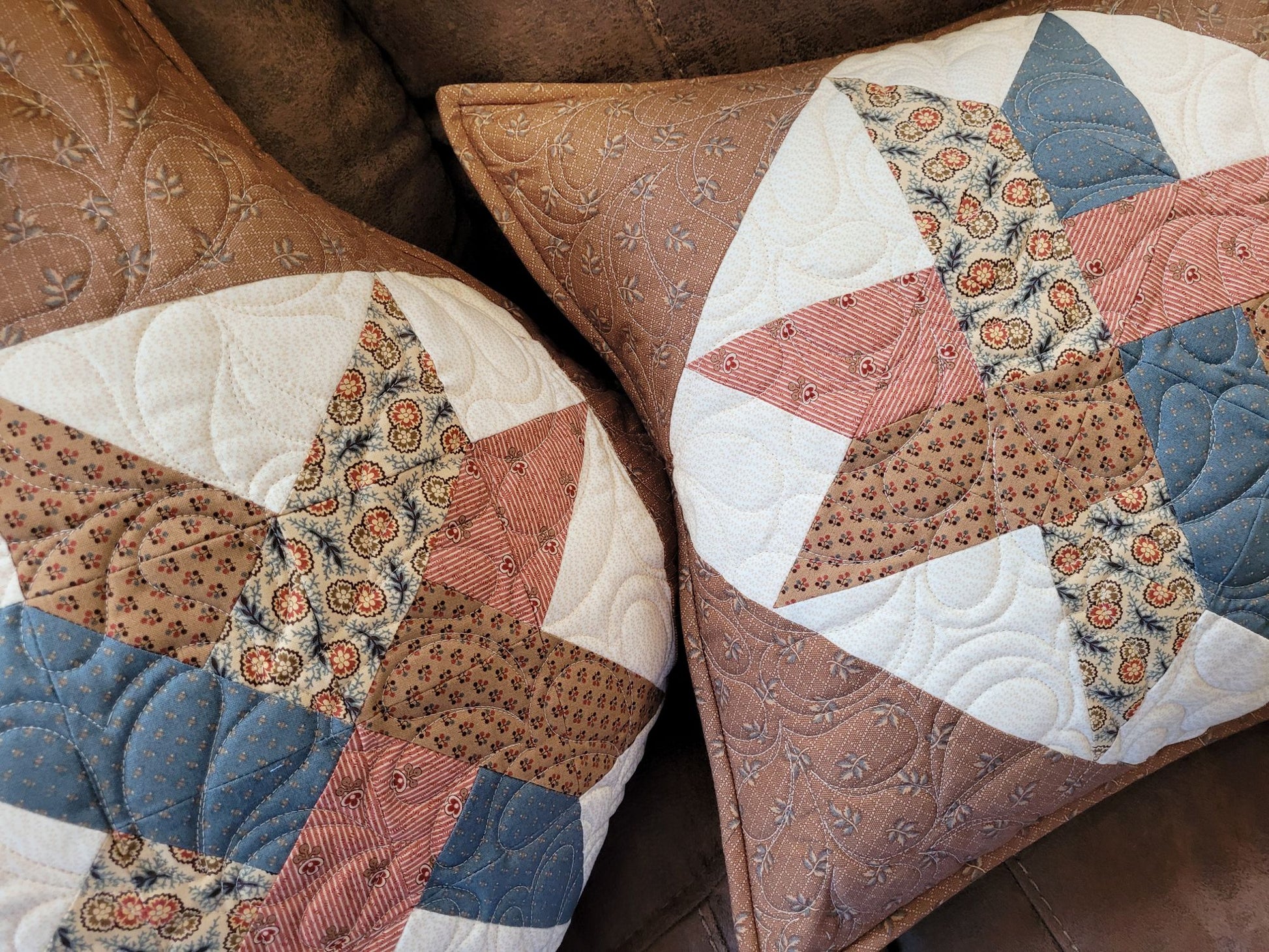 Patchwork pillows with brown, blue, red and white patterns on a couch.