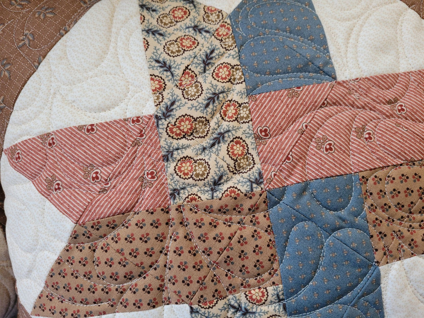 Close-up of a patchwork quilted pillow with rustic civil war reproduction fabrics in muted red, brown, blue and cream tones.