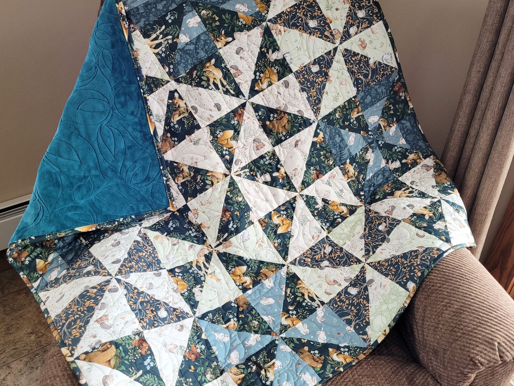 Woodland Baby Quilt with geometric pinwheel pattern draped over a chair