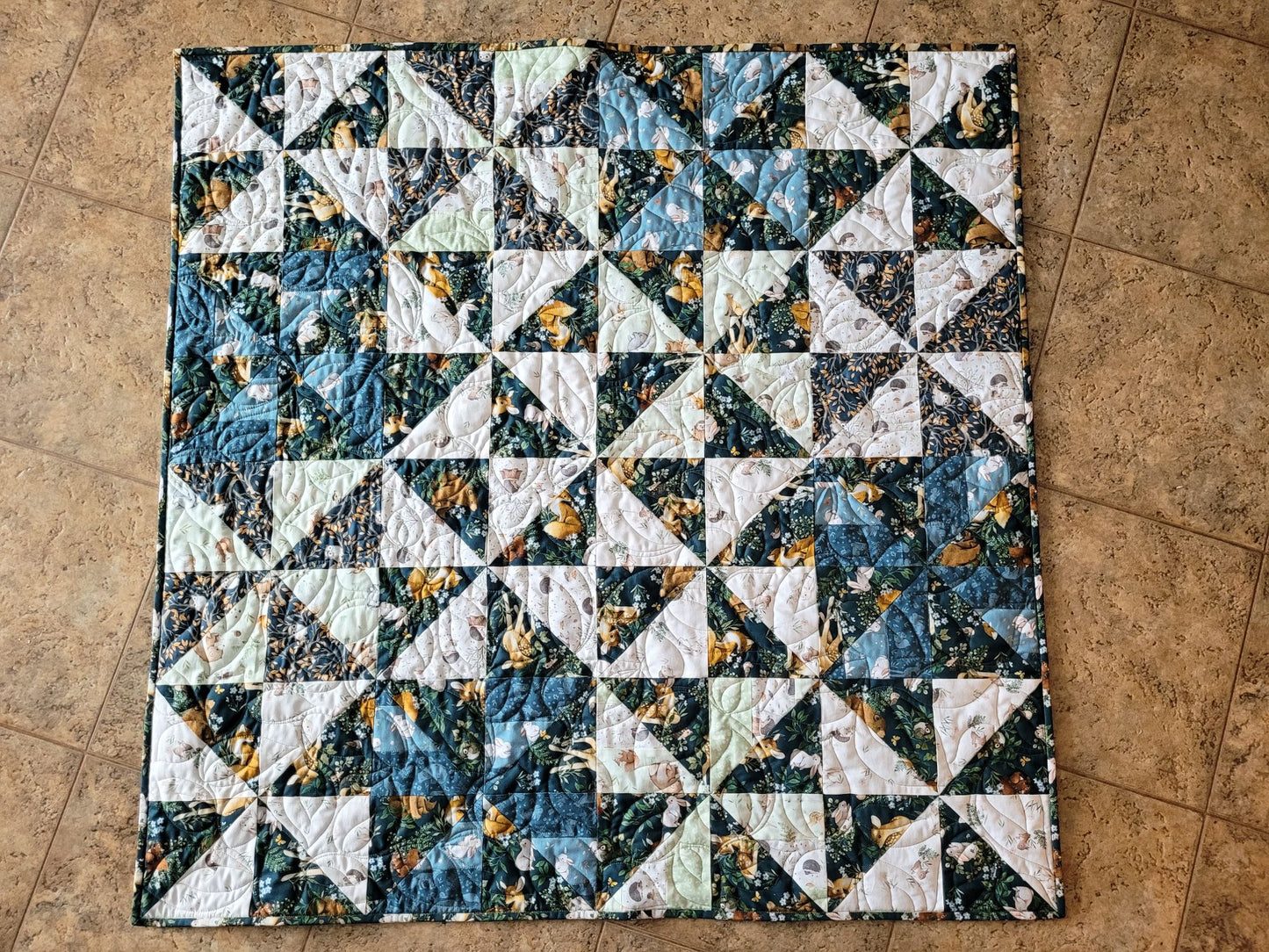 Showing the square, woodland theme baby quilt laying flat on the floor.