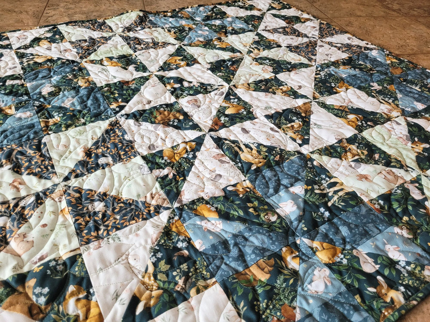 Angle view of the woodland theme baby quilt laying on the floor. 