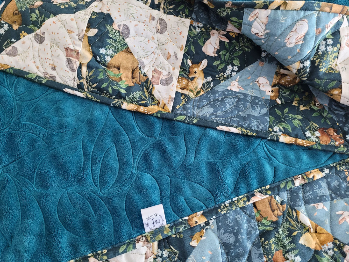 Woodland theme baby quilt close up showing the quilt folded to reveal soft backing and handmade label.