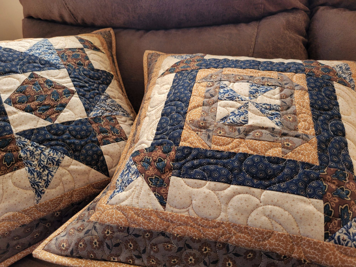Quilted pillows with a patchwork design on a brown sofa in an angled view to show quilting texture.