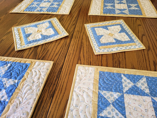 Four quilted placemats on a table with two coordinating flower hot mats.