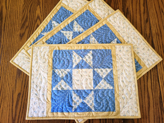 Set of four patchwork star quilted placemats in blue and beige fabrics on a wooden table.