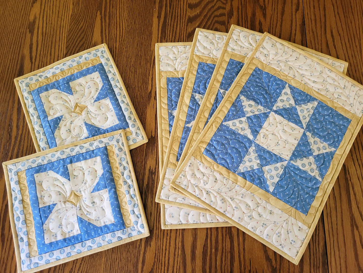 Coordinating set of four quilted placemats and two hot mats on a wooden table.
