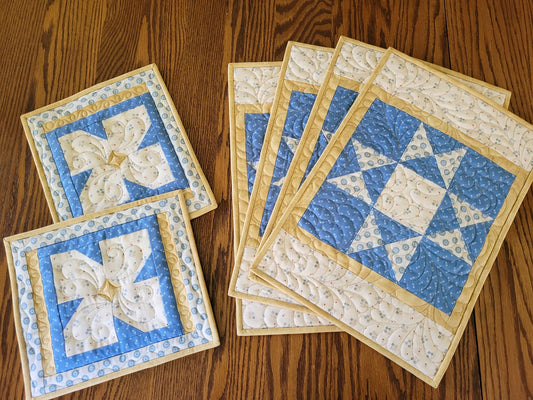 Coordinating set of four quilted placemats and two hot mats on a wooden table.