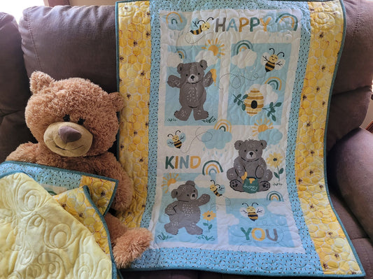 Happy bears and bees baby quilt draped on couch with a teddy bear sitting beside.
