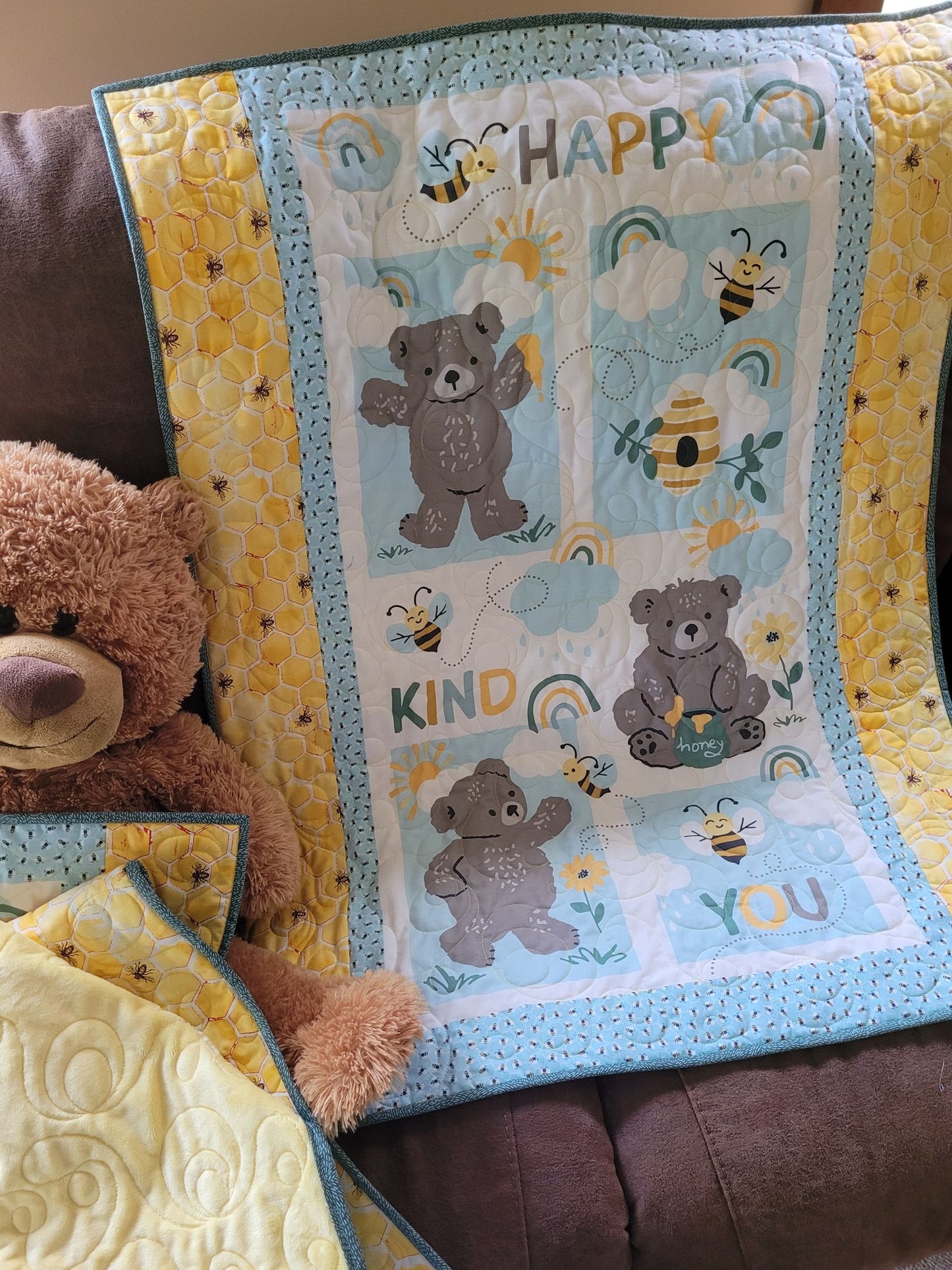 Baby quilt with bears and bees on couch with a teddy bear beside.