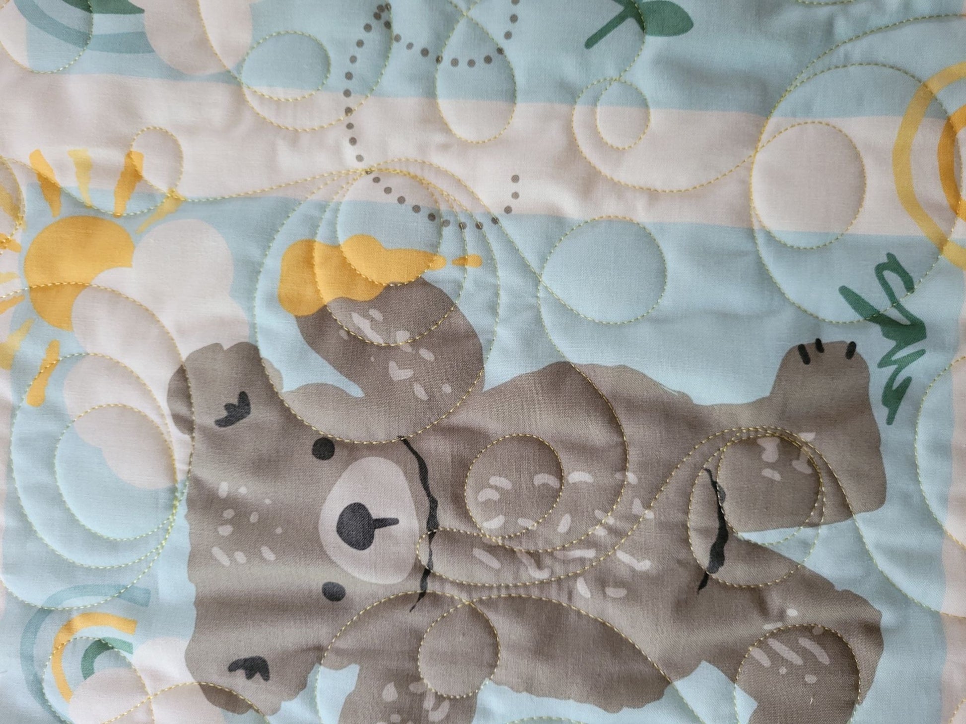 Close up details of baby quilt showing a bear with a sun behind a cloud.