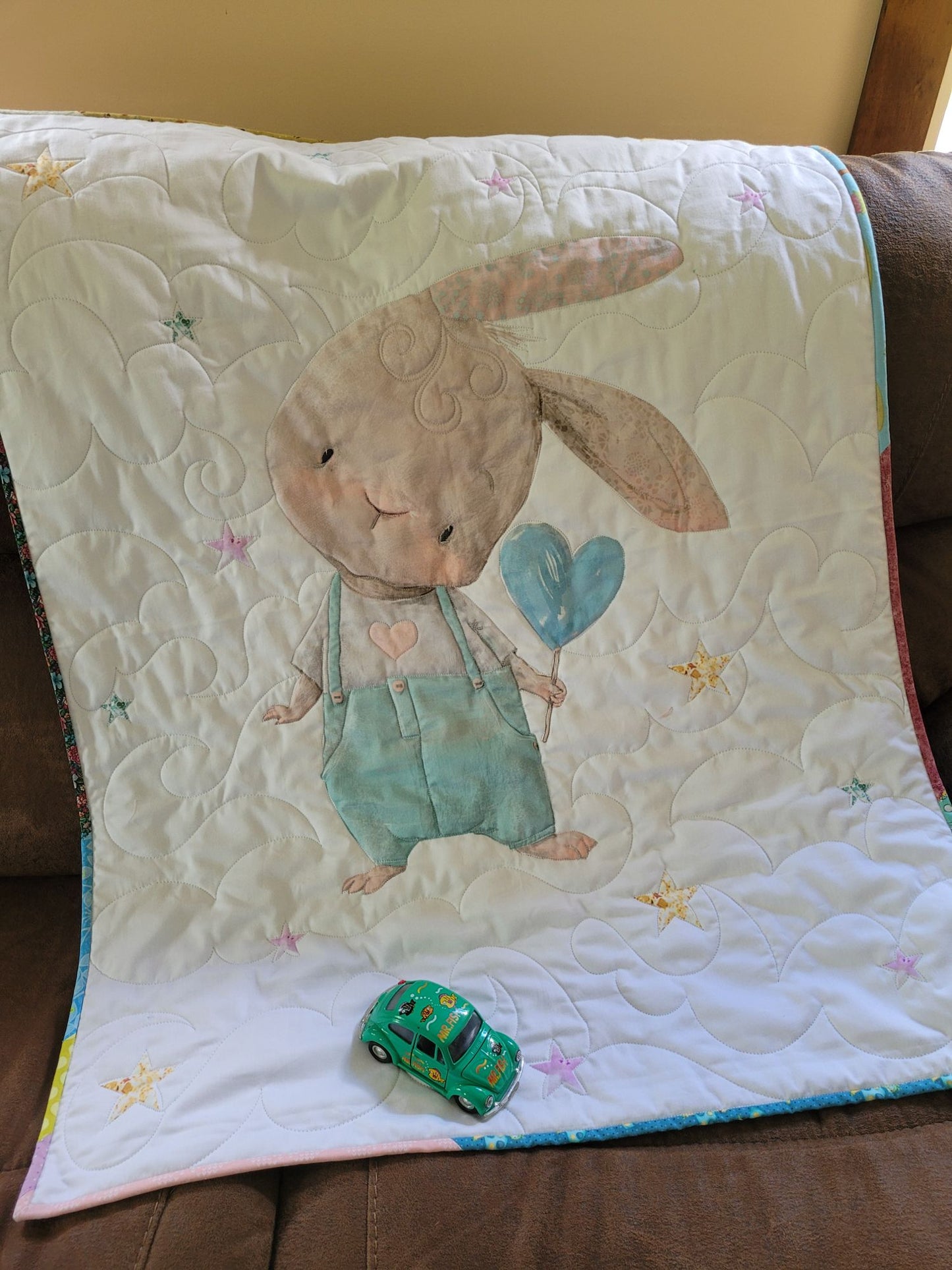 Cute shy bunny baby quilt on a couch with a toy car sitting on it.