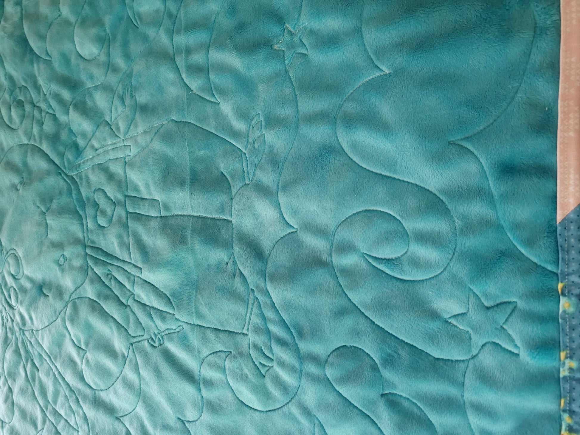 Soft teal back of bunny baby quilt showing stitching texture.