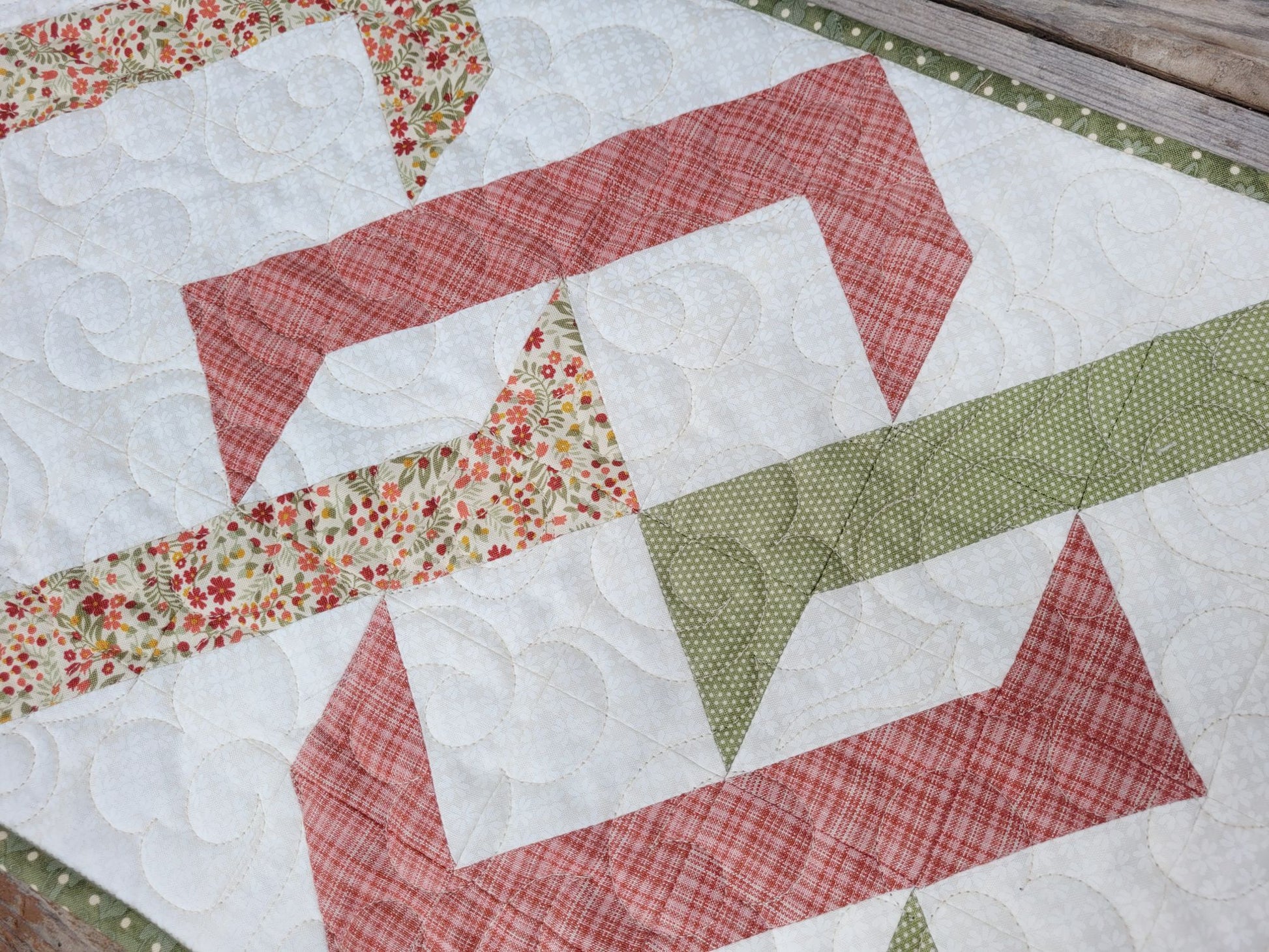 Quilt with patchwork design featuring red, white, and green fabrics on a wooden surface.