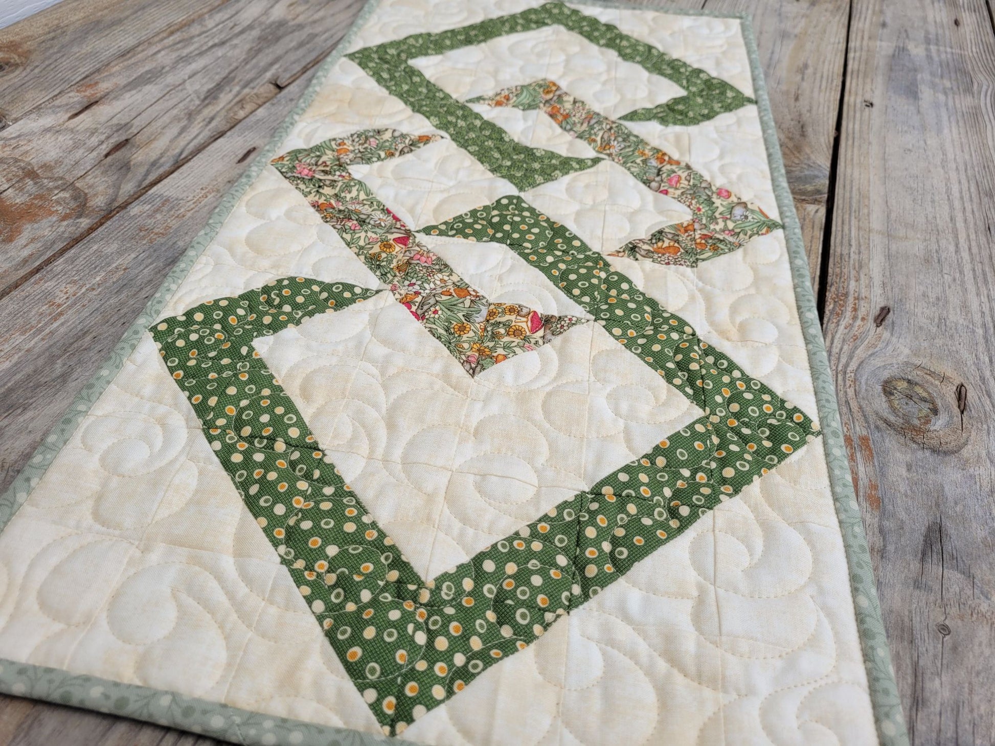 Quilted table runner with green and floral patterns on a wooden surface