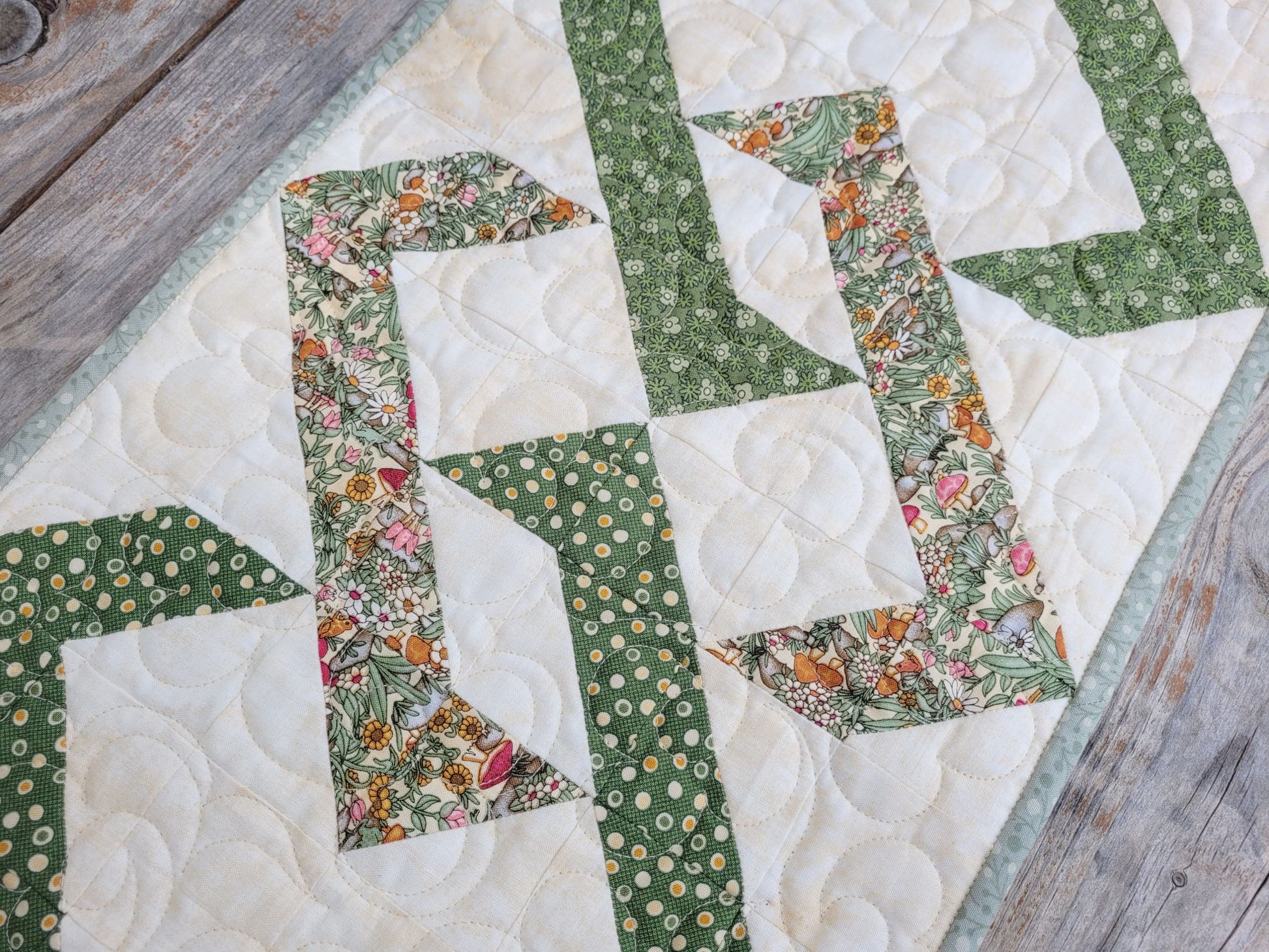 Interwoven diamond quilted table runner on wood surface. Done in green fabrics on an ecru background.