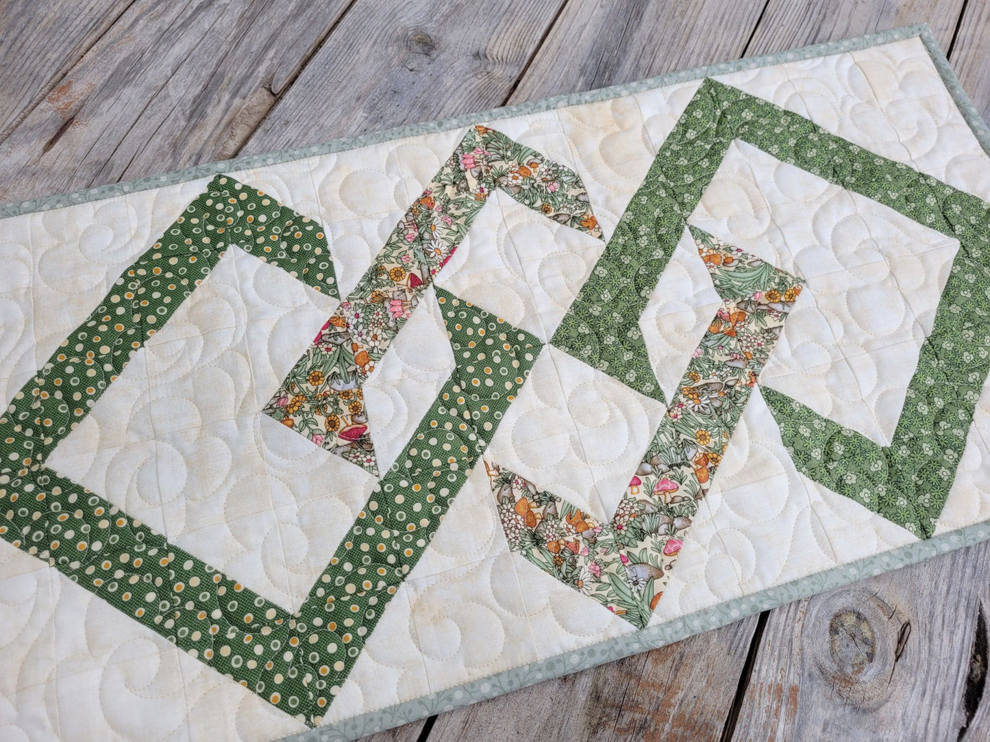 Quilted table runner with floral and geometric interwoven diamonds on a wooden surface