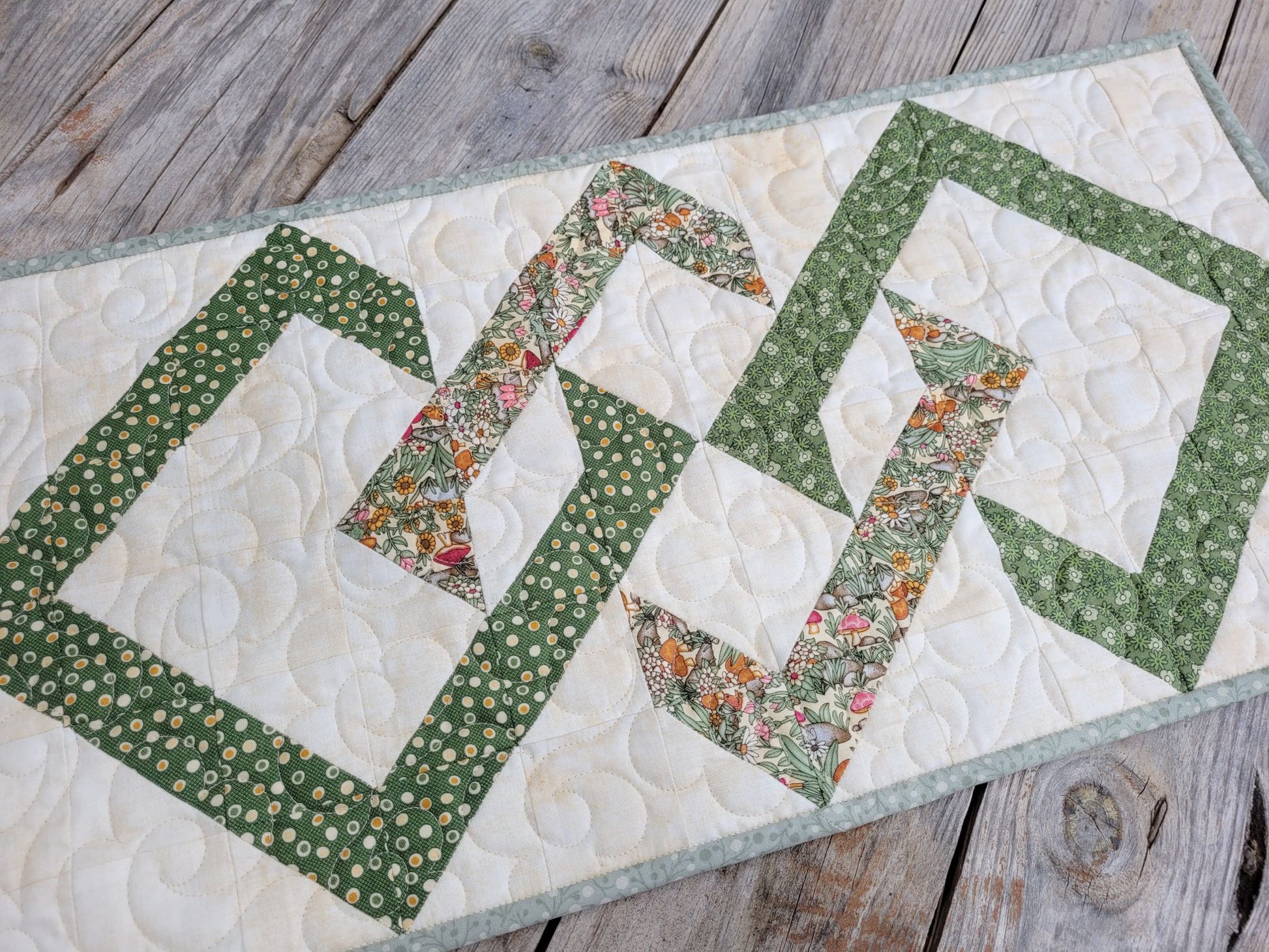 Quilted table runner with floral and geometric interwoven diamonds on a wooden surface