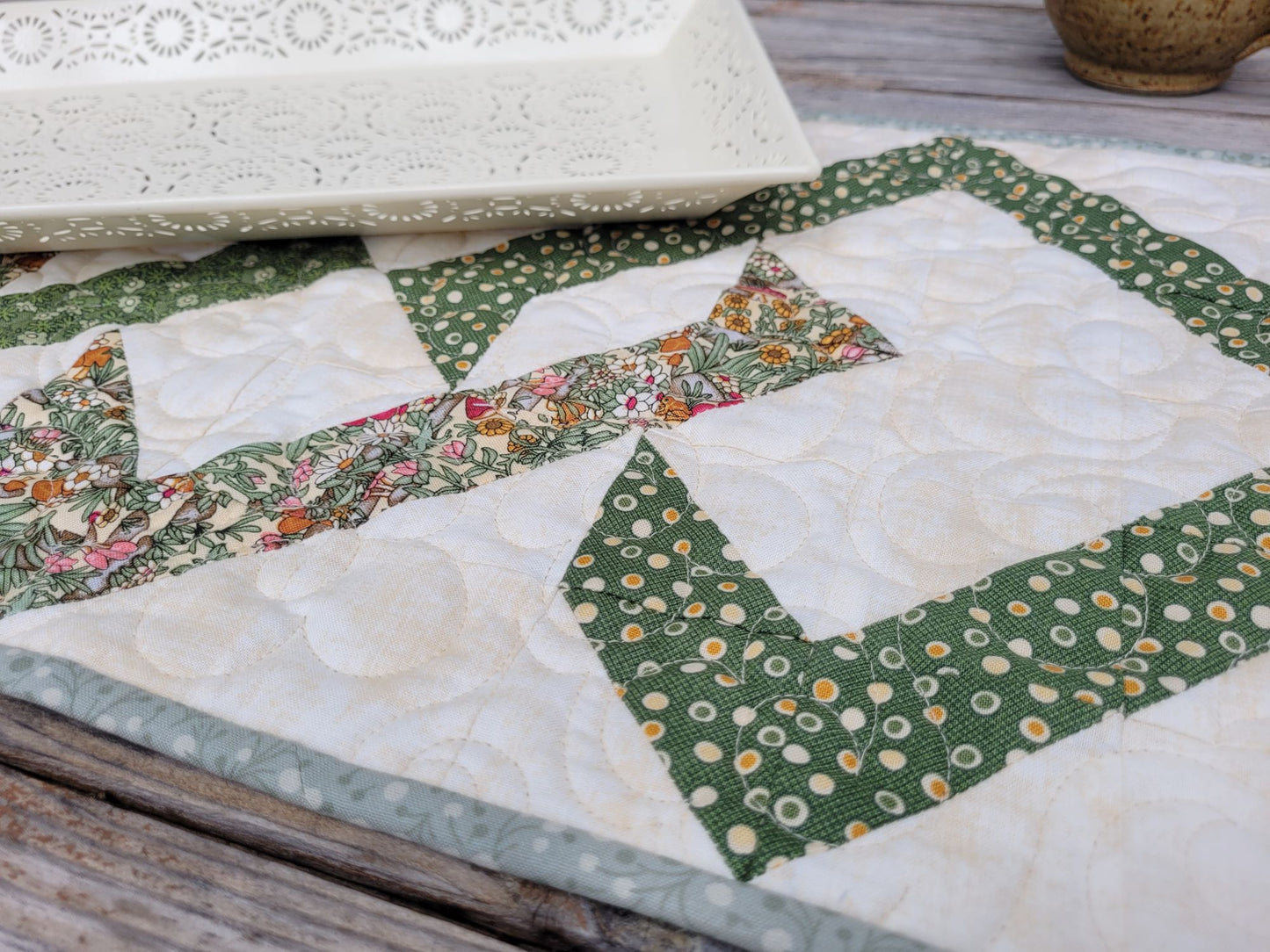 Close up of quilted table runner in green and floral fabrics on a wooden surface.
