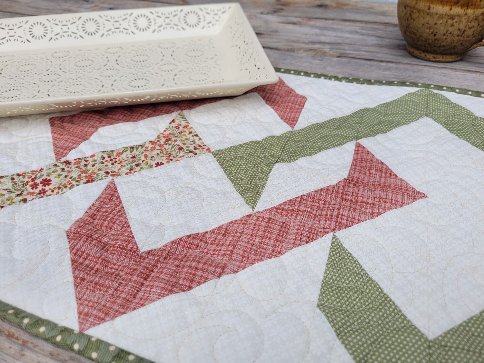 Close up of quilted table runner with white tray and mug in background.