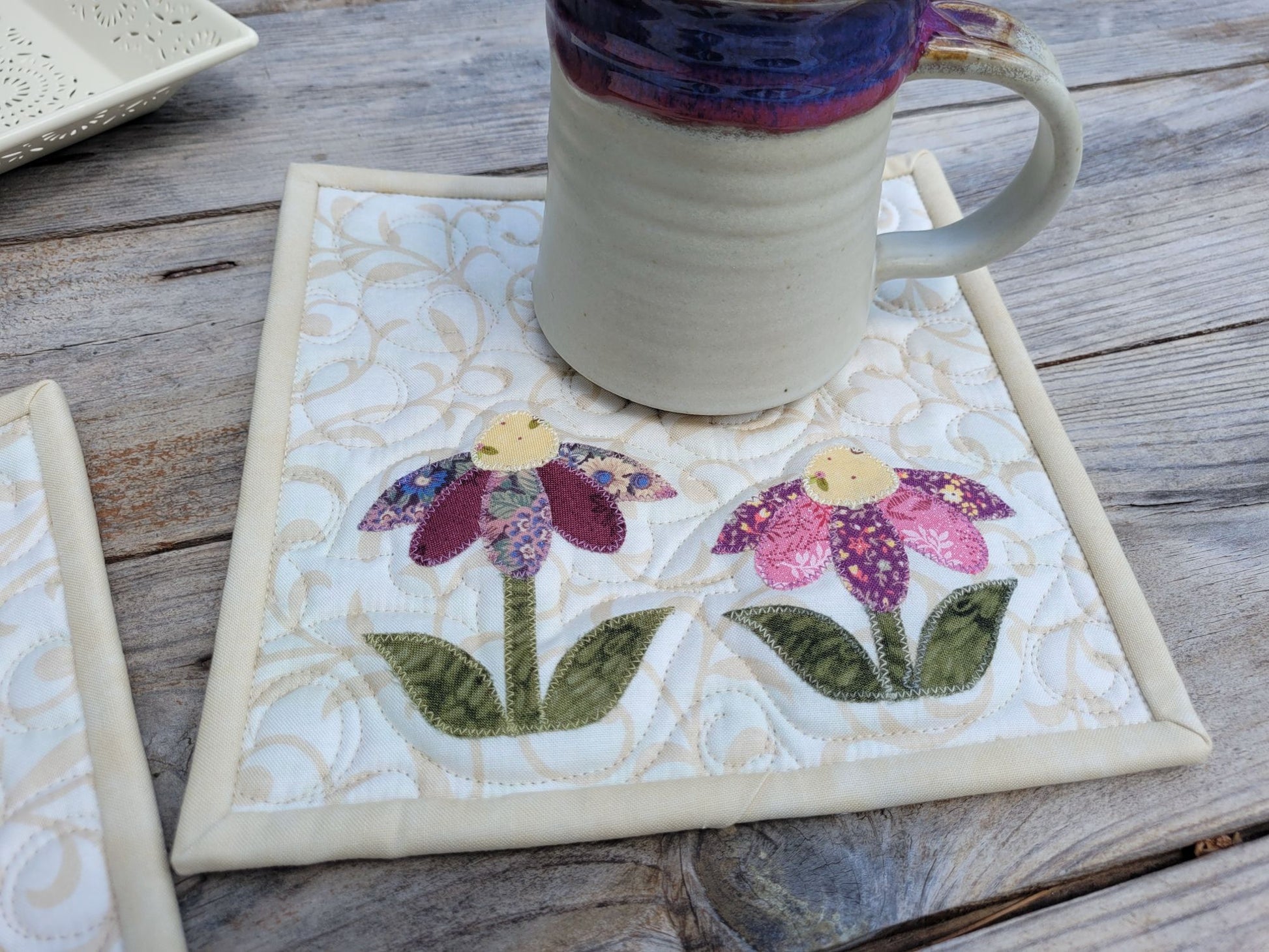 Quilted coaster with floral design holding a mug on a wooden surface