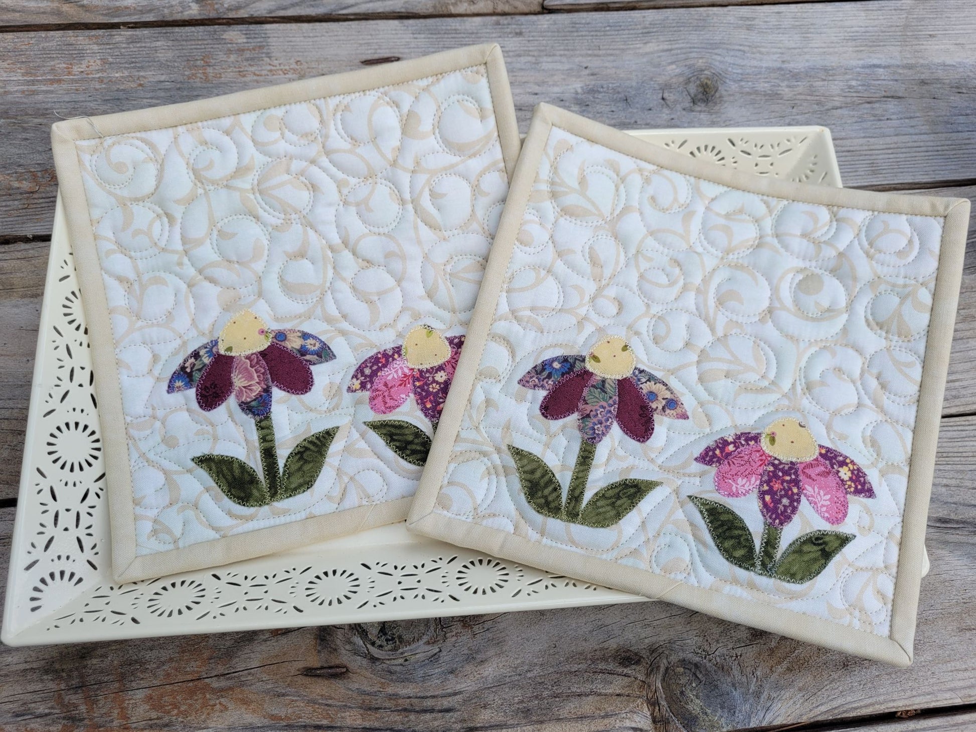 Two quilted potholders with floral designs on a wooden surface