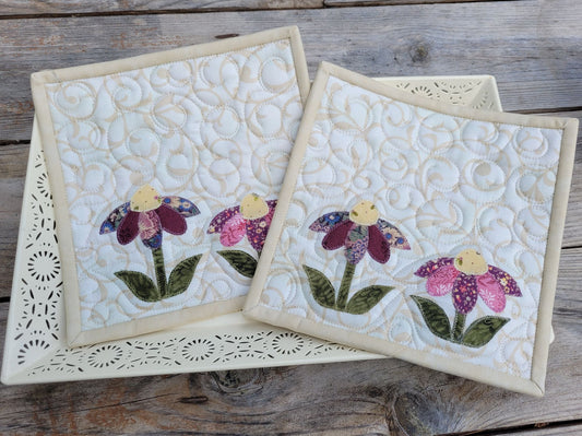 Two quilted potholders with floral designs on a wooden surface