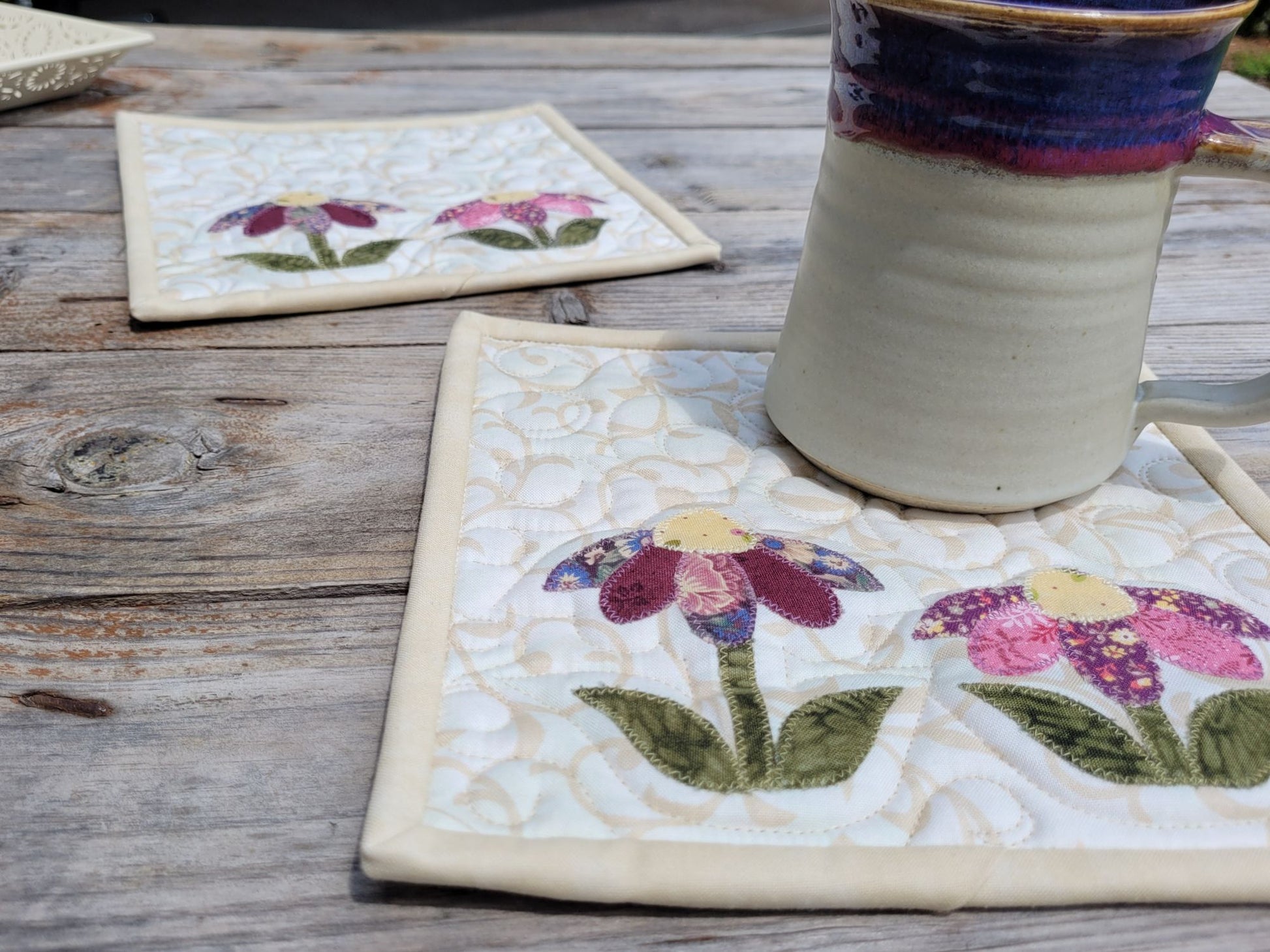 Close up angle view of quilted flower hot mats with mug, on wood table.