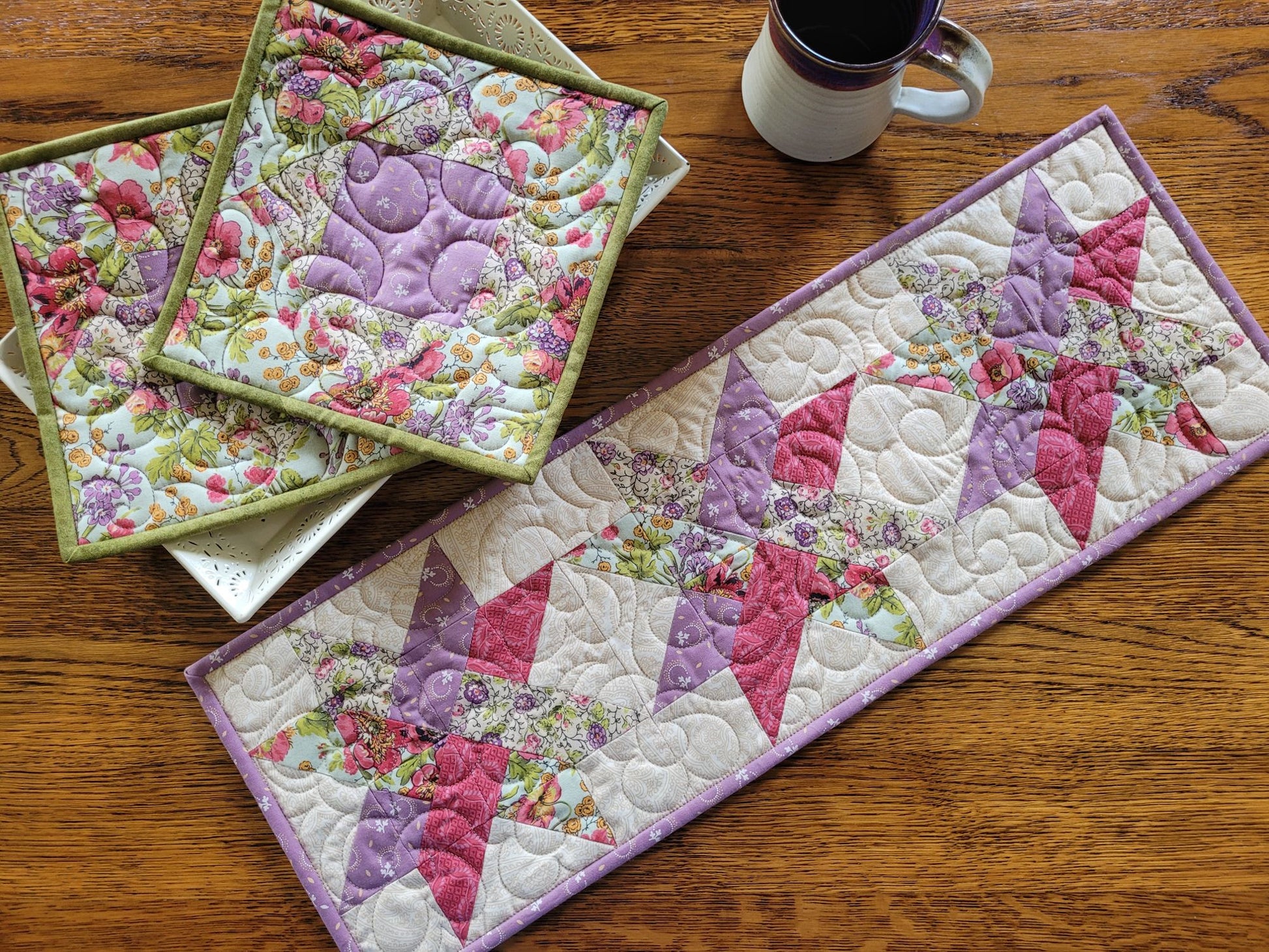 Woven star quilted table runner is shown with two coordinating hot mats on a wooden table surface with a pottery mug.