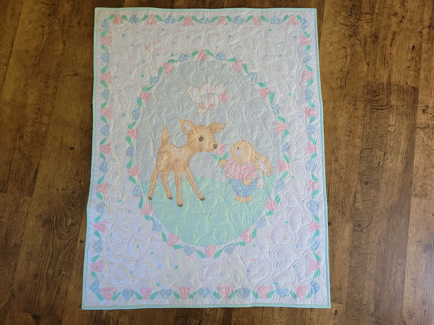 Baby quilt with a fawn and bunny on a wooden surface.