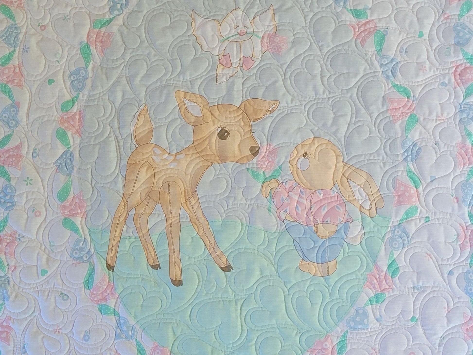 Quilt with a deer and bunny design on a patterned background.