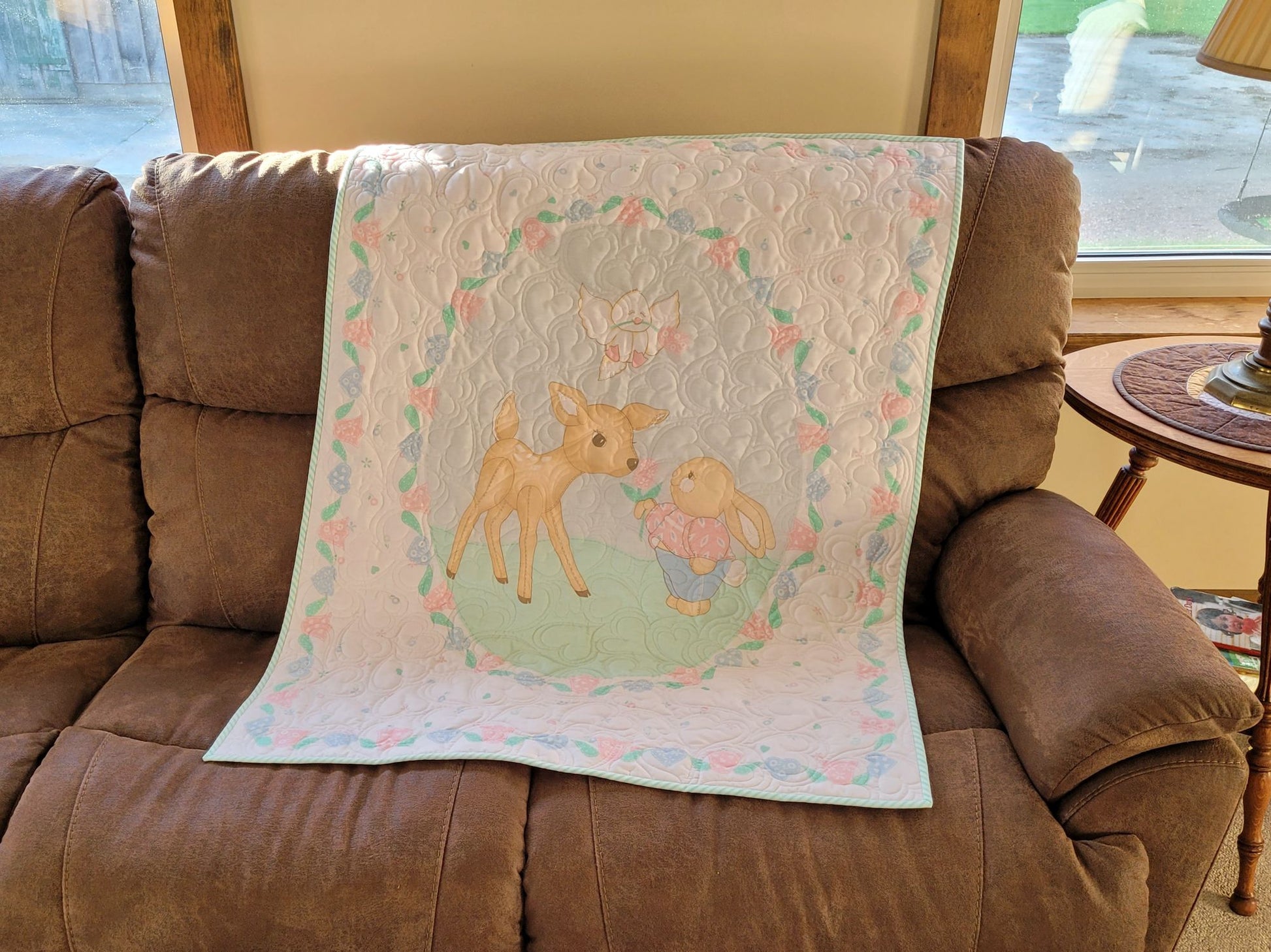 Baby quilt with a fawn and bunny on a brown couch.