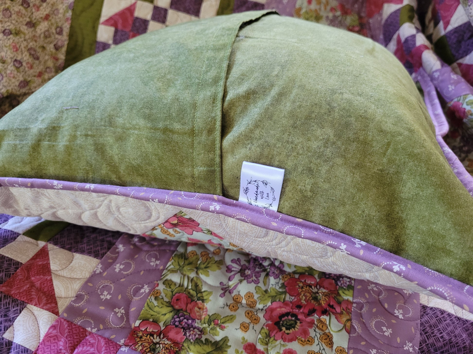 Showing the overlapping back of the quilted throw pillow in moss green fabric with small handmade label tag on side of pillow, resting on matching throw quilt.
