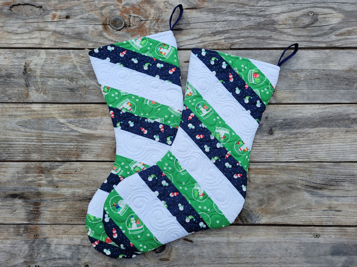 Two handmade Christmas stockings made from green, white, and navy patterned fabric, laid flat on a rustic wooden plank surface.